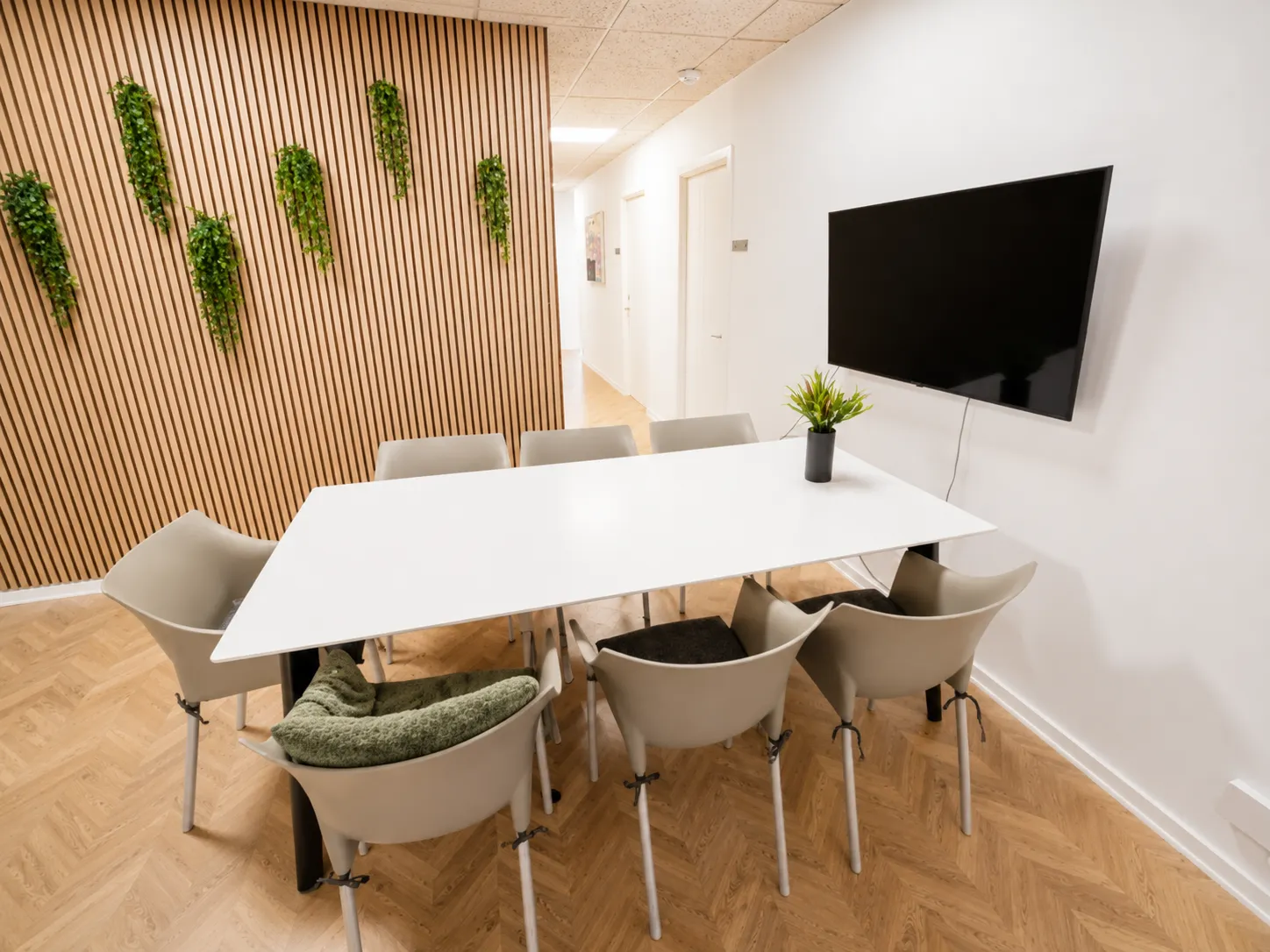 Professionelt møderum med stort hvidt bord, trævæg, planter og skærm